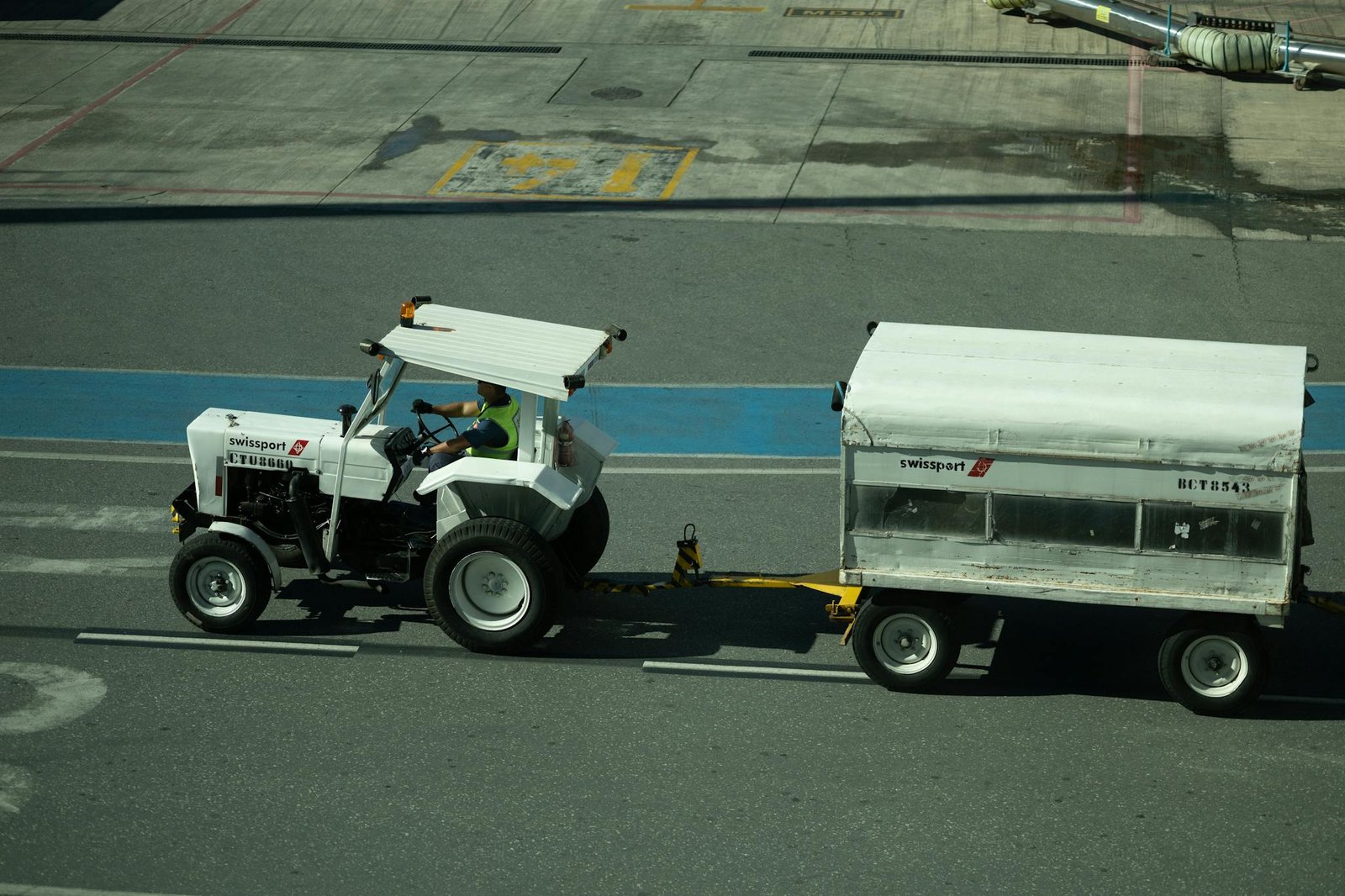 A Swissport tractor towing a trailer on an airport runway in bright daylight.
