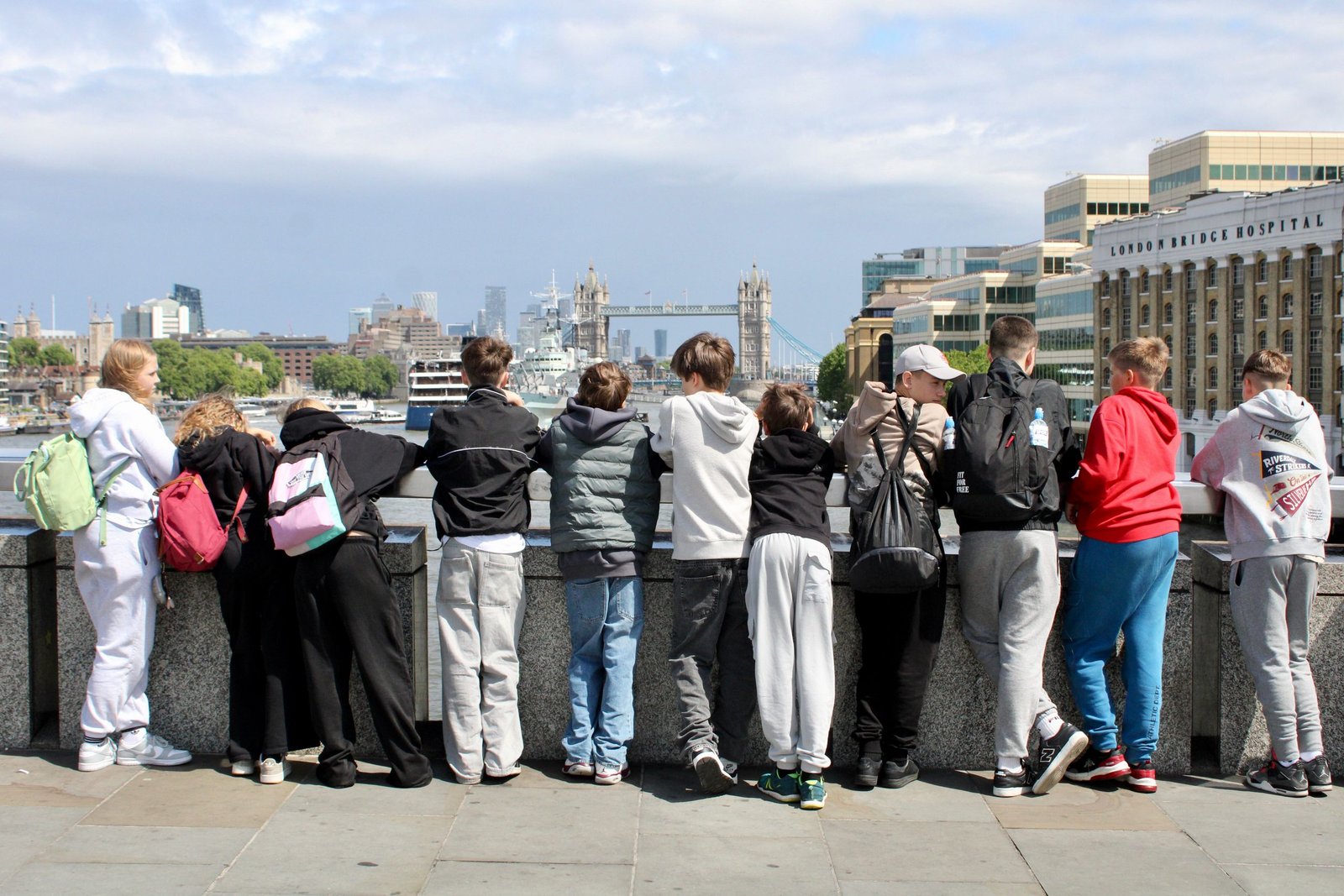 Teenagers with backpacks view Tower Bridge from a London riverside.